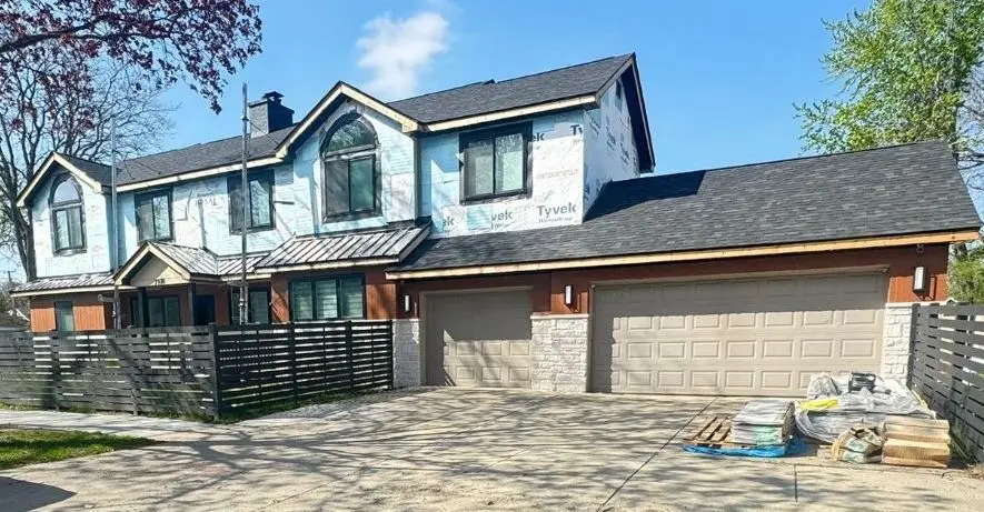 Before: two tan raised panel garage doors on a new home with stone columns