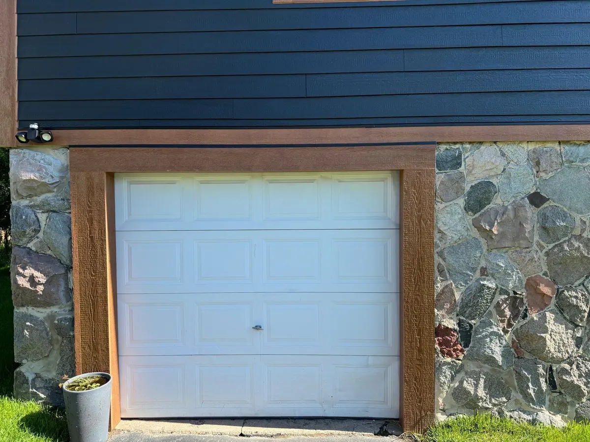 Before: plain white single garage door in a wood and stone surround