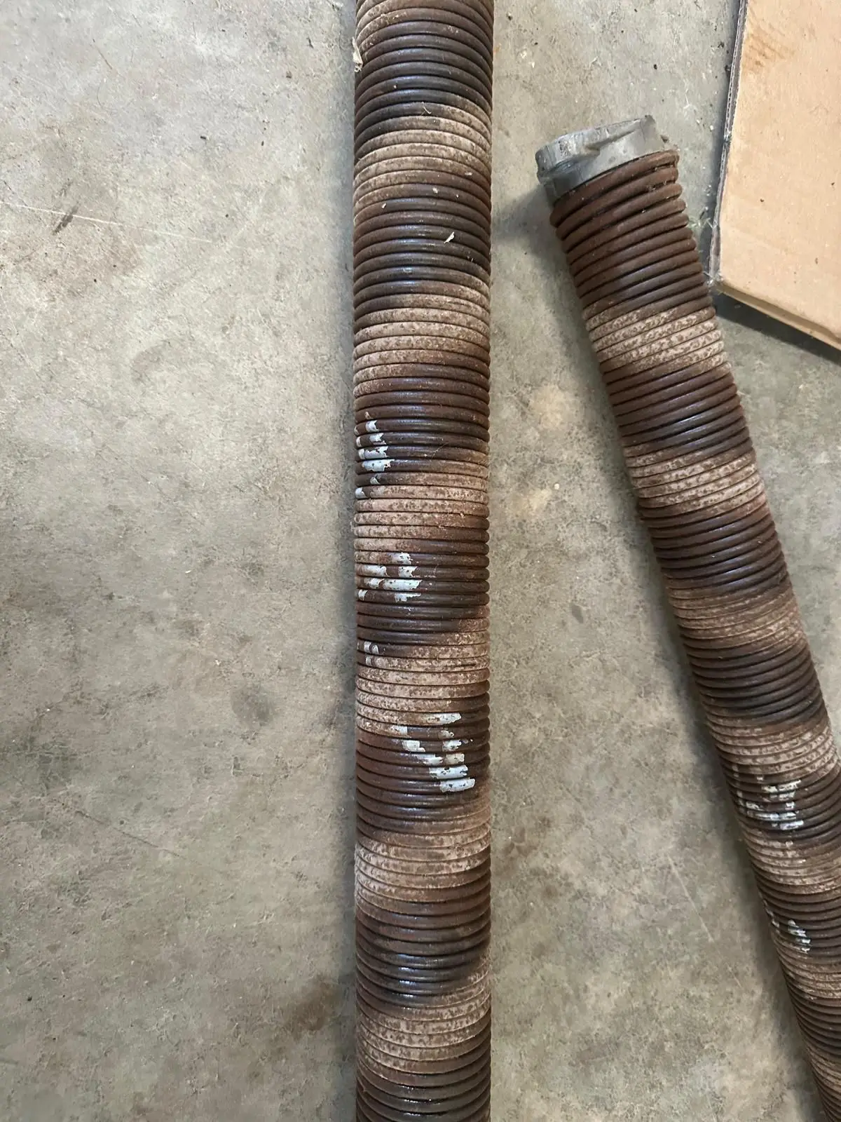 Two worn, rusted torsion springs removed from a garage door, lying on a garage floor