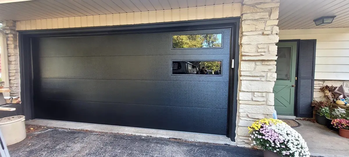 After: black modern garage door with offset windows on the same stone fronted home