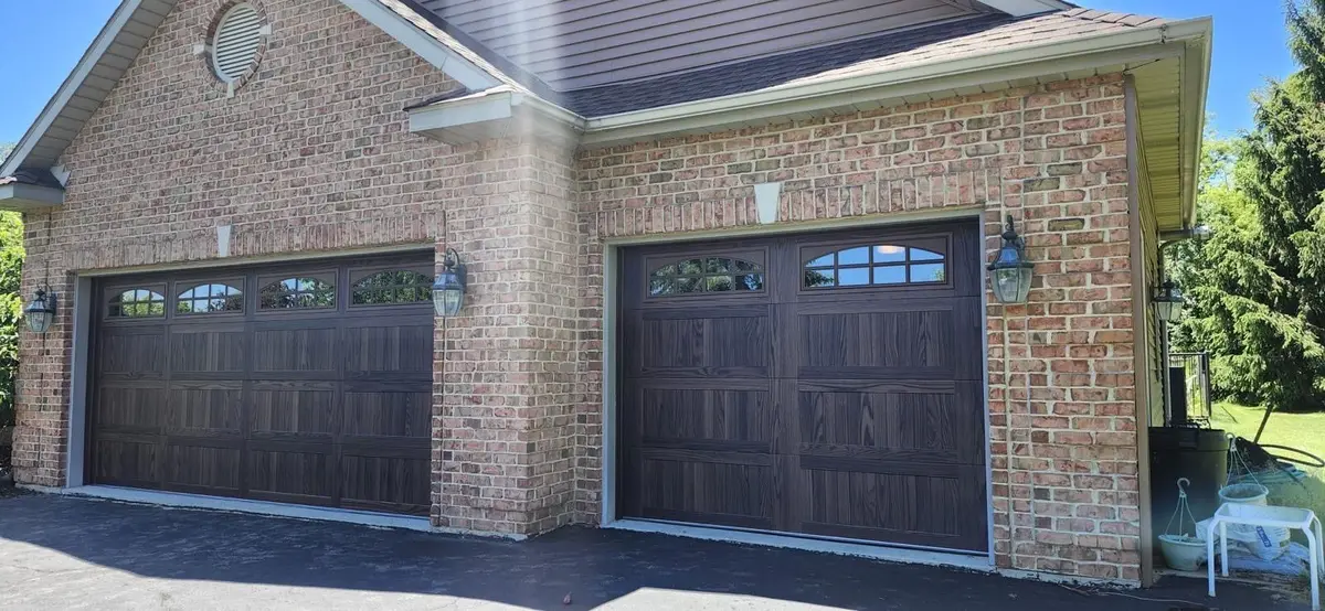 Two dark carriage style garage doors with arched windows on a brick home