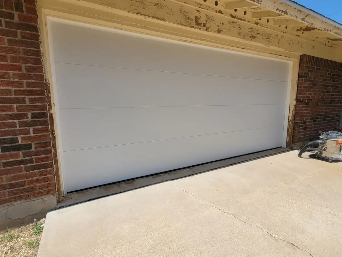 White flush panel double garage door on a brick home