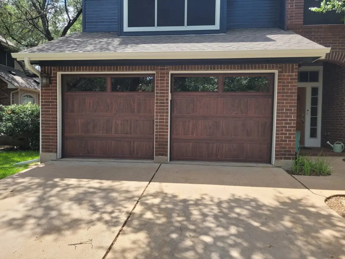 Two wood tone carriage style garage doors with windows on a brick Austin home, installed by Tier One