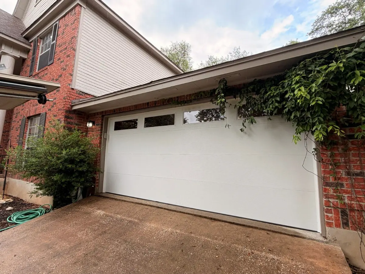 White flush panel garage door with a row of top windows on a brick Austin home, installed by Tier One