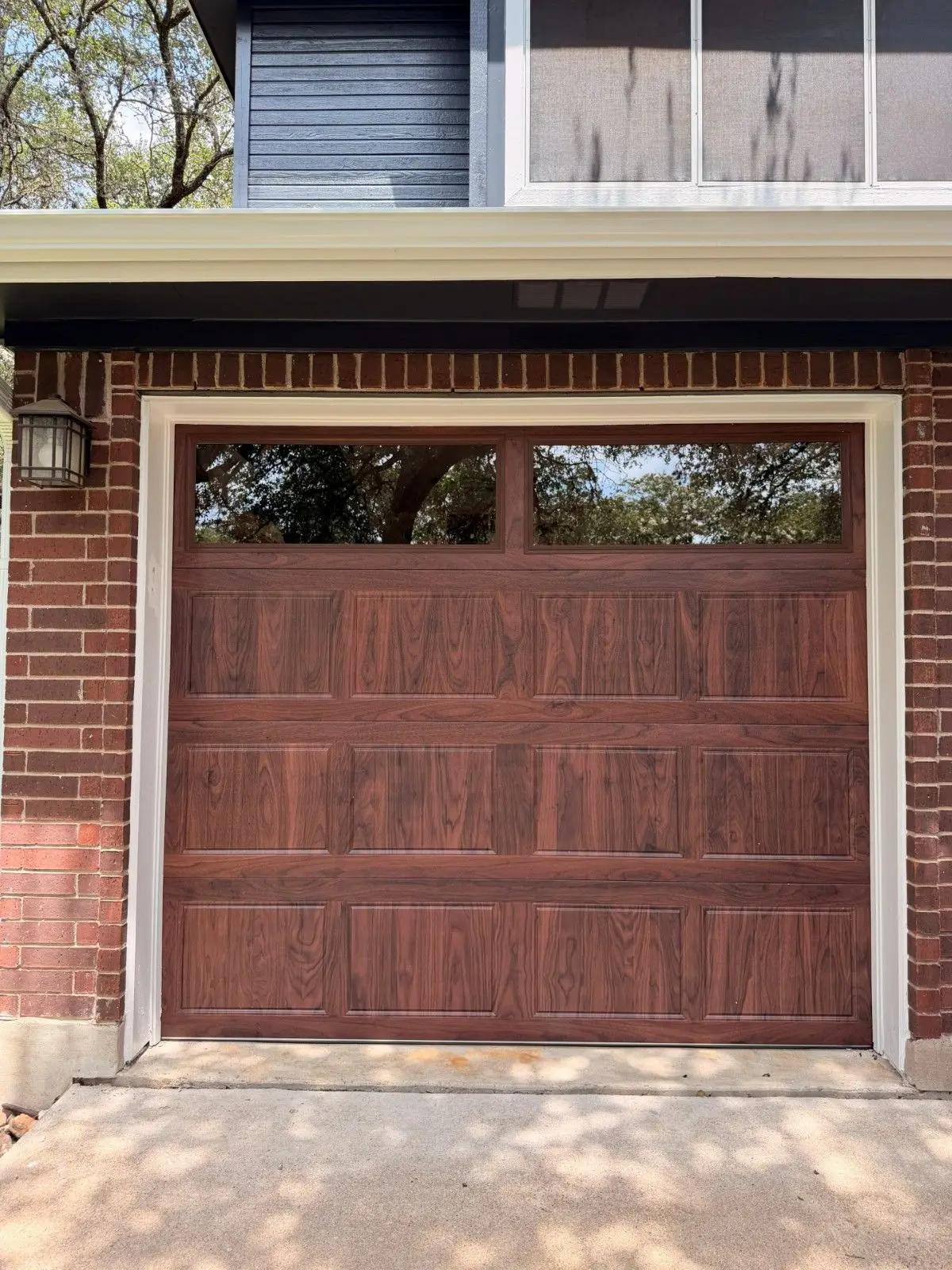 Wood tone raised panel garage door with top windows on a red brick home, installed by Tier One