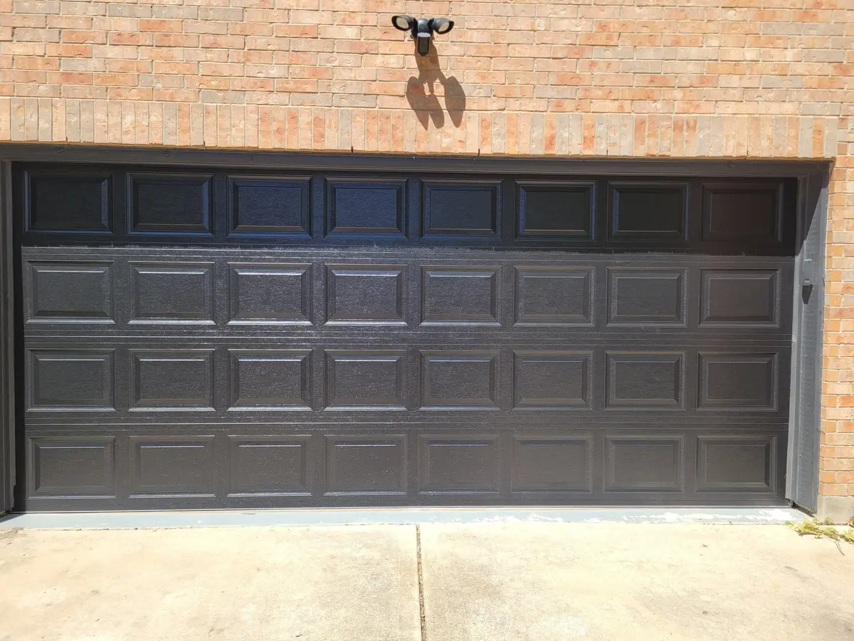 Black raised panel double garage door on a brick Pflugerville home, installed by Tier One