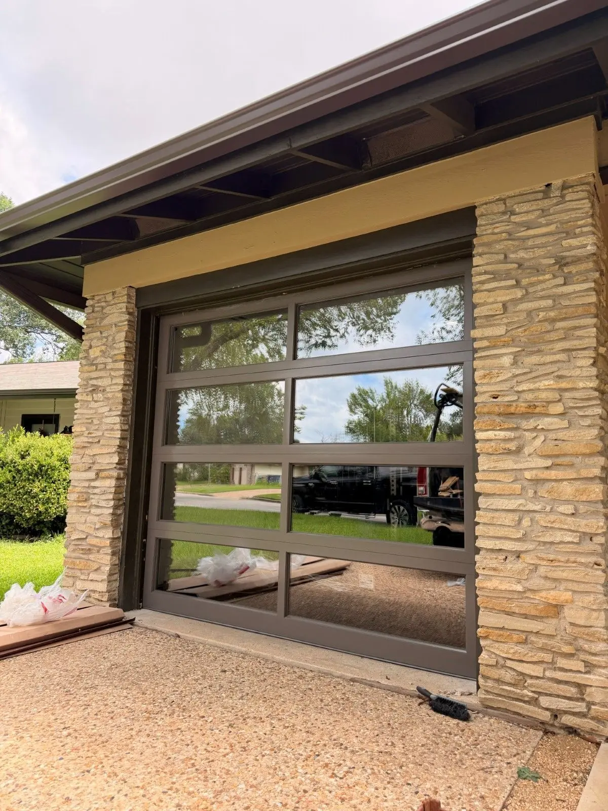 Bronze framed full view glass garage door between stacked stone columns, installed by Tier One
