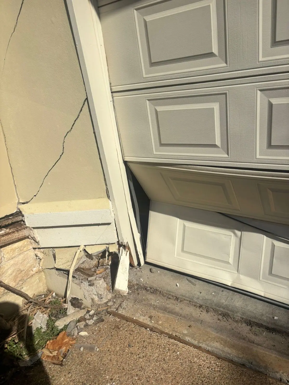 Garage door bottom corner pushed in, with the door frame and wall damaged by an impact