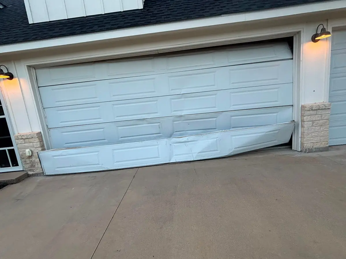 White garage door with its bottom sections buckled inward after an impact