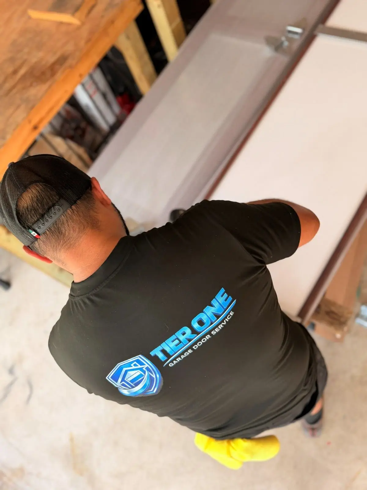 Tier One technician kneeling to work on the bottom of a garage door track